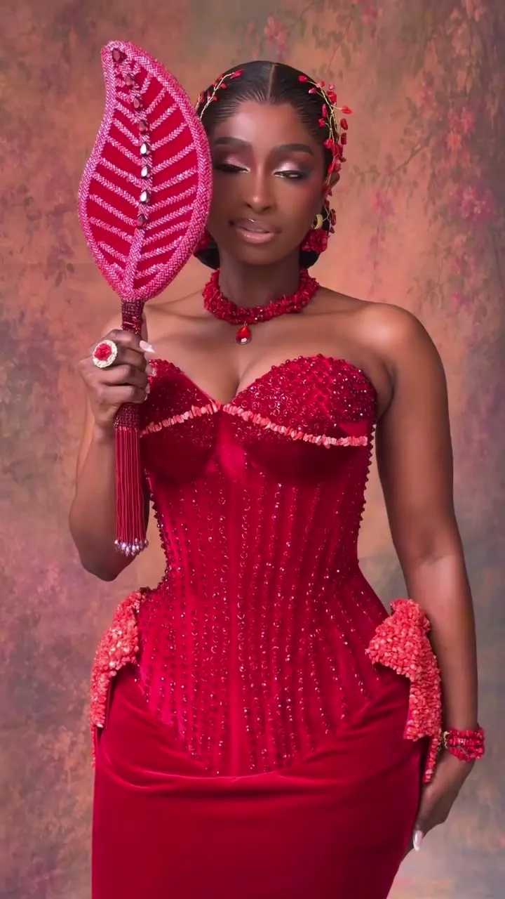 Kossy in a red beaded corset gown holding a leaf fan