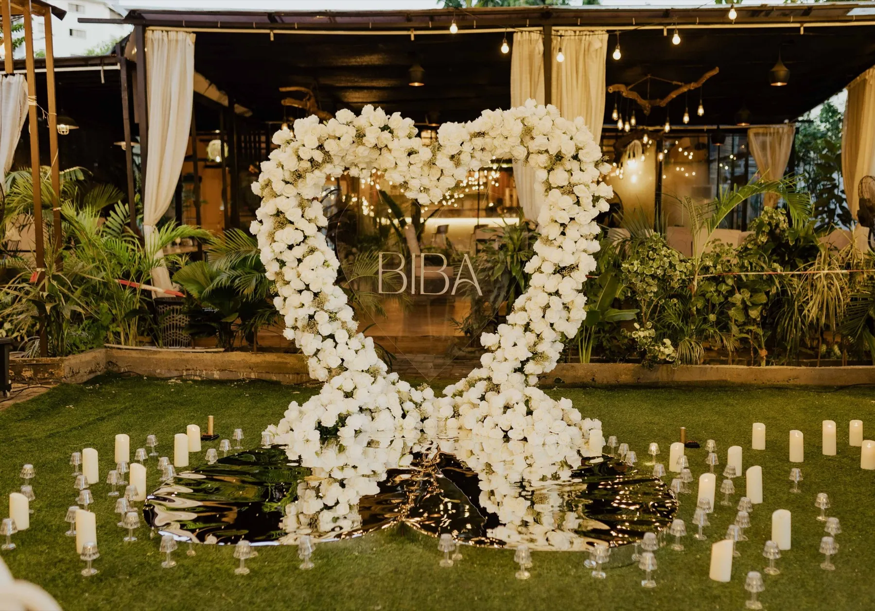 A white floral heart surrounded by candles at dusk
