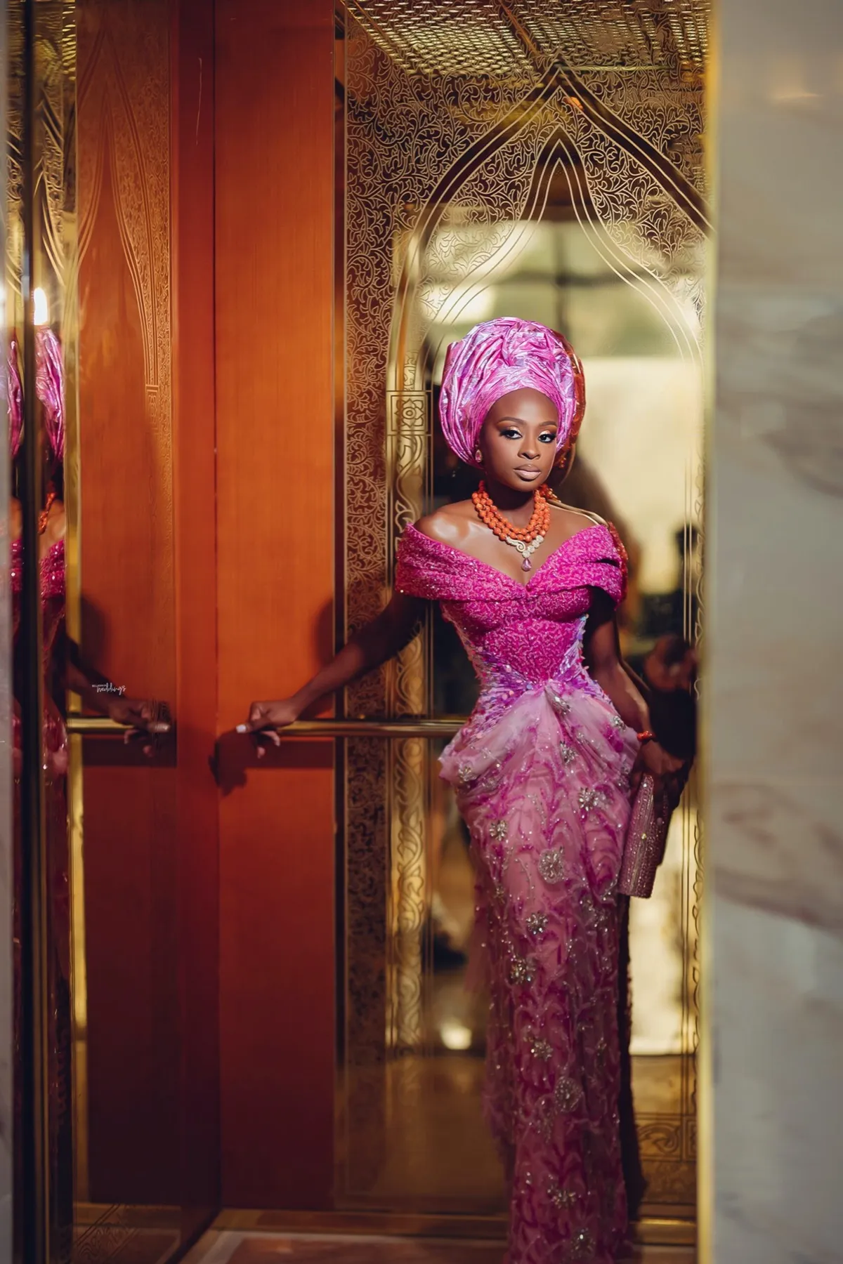 Lade in pink aso oke at a gold doorway